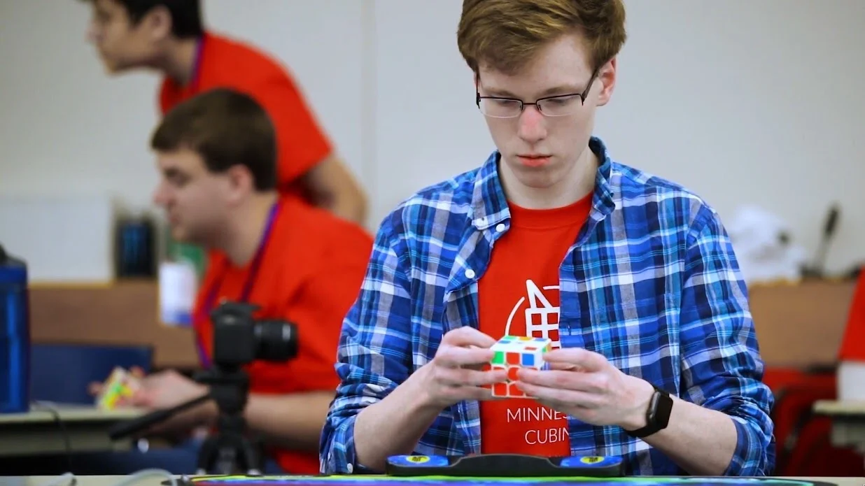 Kennan, in a plaid shirt, mid-solve at a speedcubing competition